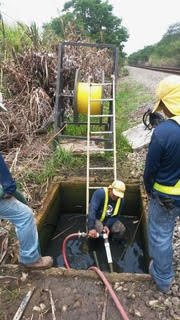Personal técnico trabajando en cámara soterrada con ducto para fibra óptica paralelo a vía ferroviaria